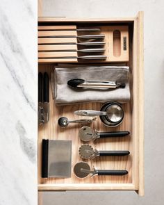 an open drawer with utensils and other kitchen items in it on a marble countertop