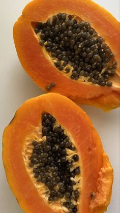 two pieces of papaya on a white surface with seeds in the middle and one half cut open