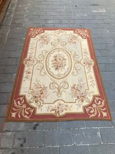 an area rug on the side of a brick road with a red border around it