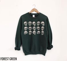 Skulls Halloween Crewneck Sweatshirt  This fabulous graphic will be printed on a Gildan 18000 Unisex Sweatshirt which runs true to size. If you are looking for an oversized fit, we recommend sizing up. Please refer to the size chart in the images. We use professional quality DGT printing on all our apparel. Direct-to-garment, or DTG, is a high quality printing method that sprays ink directly onto the garment so there is no peeling or cracking. Estimated Production Time: 1-5 days Estimated Shippi Green Band Merch Top For Fall, Relaxed Fit Skull Print Tops For Winter, Halloween Skull Sweatshirt In Black, Winter Skull Print Relaxed Fit Tops, Halloween Cotton Sweatshirt With Skull Design, Halloween Skull Print Crew Neck Sweater, Halloween Crewneck Sweatshirt, Halloween Skulls, Skeleton Sweatshirt