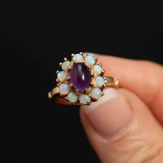 Elevate your style with this exquisite 10K gold cocktail ring, a true testament to the artistry of fine jewelry craftsmanship. This stunning piece features a mesmerizing 8mm oval cabochon amethyst at its center, encircled by ten fiery 2.5mm opals that dance with a captivating play of colors. The focal point of this ring is the 8mm oval cabochon amethyst, a regal gem known for its deep, rich purple hue. Surrounding the amethyst are ten 2.5mm opals that exhibit a fiery play of colors, making this Luxury Amethyst Ring With Oval Cabochon, Elegant Amethyst Cabochon Ring, Elegant Purple Cluster Ring For Formal Occasions, Purple Gemstone Cluster Ring For Formal Occasions, Elegant Yellow Gold Cabochon Amethyst Ring, Elegant Yellow Gold Amethyst Cabochon Ring, Formal Purple Gemstone Cluster Ring, Elegant Gold Amethyst Cabochon Ring, Elegant Purple Cluster Ring For Anniversary