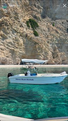 a white boat floating on top of a body of water next to a rocky cliff