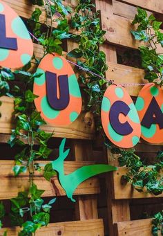 some orange and green paper letters are hanging from a wooden fence with ivy on it