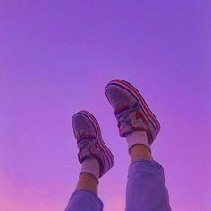 a person with their feet up in the air wearing tennis shoes and jeans, against a purple sky