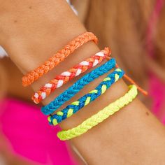 four different colored bracelets on a woman's arm, one is orange, the other is blue