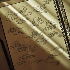 an open notebook with drawings on it and some clouds in the sky over water below