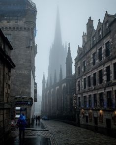 people are walking down the street in front of old buildings on a foggy day