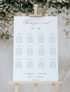 an easel with a seating chart on it and greenery in the back ground