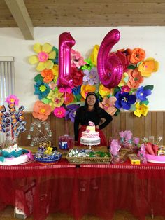 a woman standing in front of a table filled with balloons and cake on top of it