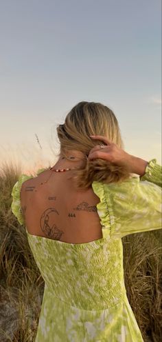 a woman with tattoos on her back standing in tall grass and looking at the sky