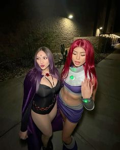 two women dressed in costumes standing next to each other on a sidewalk at night time