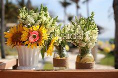 three vases with sunflowers and other flowers are sitting on a table outside