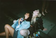 two young women sitting on the ground with their mouths open and one holding a cell phone