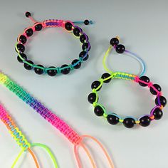 three bracelets with black beads and multicolored string on white background, one is for children