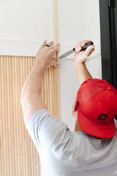 a man in a red hat is holding a pair of scissors and cutting the wall