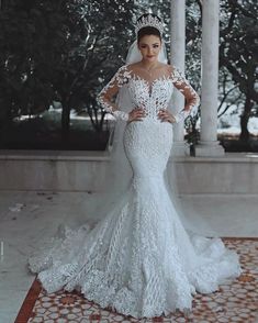 a woman wearing a wedding dress with long sleeves and a veil on her head standing in front of columns