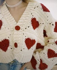 a woman wearing a red and white crochet sweater with hearts on the sleeves