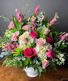 a white vase filled with lots of pink and white flowers on top of a wooden table