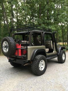 a jeep with its doors open parked in the middle of a gravel road next to trees