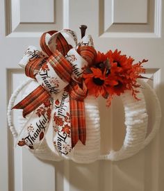 a white pumpkin wreath hanging on the front door with fall decorations and ribbon around it