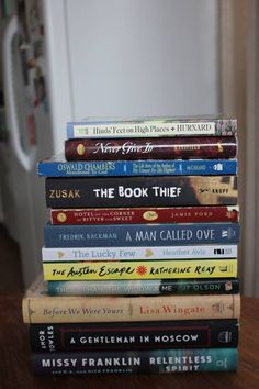 a stack of books sitting on top of a wooden table in front of a refrigerator