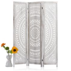 a white room divider next to a vase with sunflowers on the table