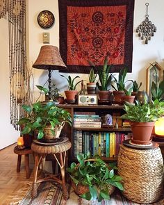 some plants are sitting in front of a wall hanging over a book shelf and two wicker stools