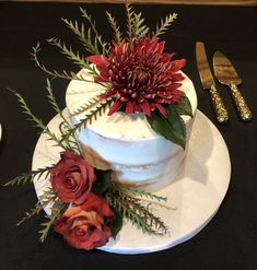 a white cake with red flowers and greenery on top, sitting on a table