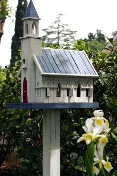 a white birdhouse with a blue roof and a red door on it's side