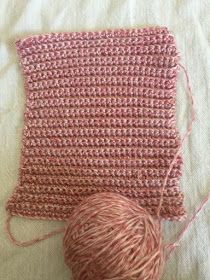 a ball of yarn sitting on top of a bed next to a pink crocheted pillow