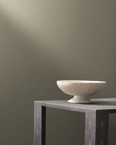 a white bowl sitting on top of a wooden table next to a wall with a light coming through the window