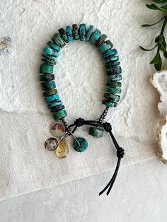 Something bold to wear on its own or with a stack. The beautiful blues and greens of these turquoise beads are perfectly complimented with Citrine and Smokey Quartz charms along with black Hematite spacers. This Boho style bracelet measures 7 1/2"-8 1/2". This will fit a 6" wrist loosely (see video). Turquoise beads are 10mm wide and variety of thicknesses. Hematite beads are 1mm flat, 2mm round. Leather in Black or Brown is 1.5mm thick. TLC brand tag 12mm. Facted Citrine briolette is 10x15mm. S Bohemian Turquoise Wrap Bracelet With Gemstone Beads, Bohemian Turquoise Gemstone Beads Wrap Bracelet, Turquoise Gemstone Beaded Bracelets For Festivals, Healing Turquoise Wrap Bracelet With Gemstone Beads, Bohemian Turquoise Stone Bracelet, Handmade Turquoise Leather Bracelet Spiritual, Artisan Turquoise Bracelets With Large Beads, Green Bohemian Beaded Bracelets With Stones, Bohemian Green Beaded Bracelets With Stones