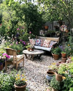 an outdoor seating area with potted plants and flowers on the ground, in front of a wooden fence