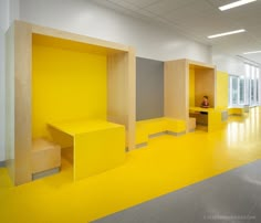 an empty room with yellow walls and benches on the floor, in front of large windows