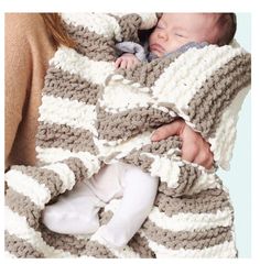 a woman is holding a baby wrapped in a crochet blanket while she sleeps