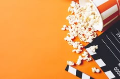 popcorn spilled out of a bucket next to a clapper and movie ticket on an orange background