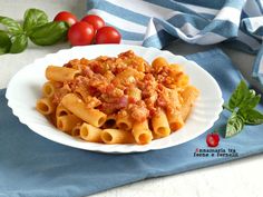 a white plate topped with pasta covered in sauce next to tomatoes and green basil leaves