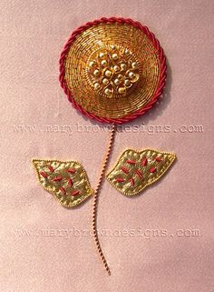 a red and gold brooch sitting on top of a pink table next to a pair of scissors