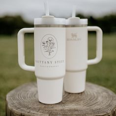 two white coffee cups sitting on top of a wooden stump