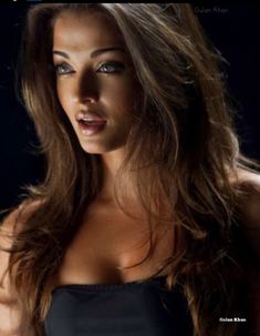 a woman with long brown hair wearing a black top and posing for the camera in front of a dark background