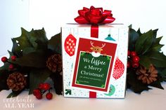 a white box with a red bow on top of it and christmas decorations around it