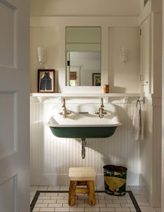 a bathroom with a sink, mirror and stool in the corner next to it's door