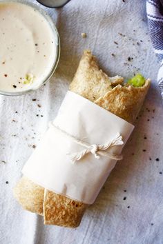 a wrapper wrapped in white paper next to a cup of coffee on a table