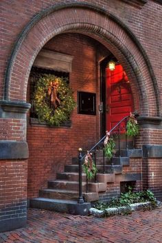 a brick building with stairs and wreaths on the front door, next to an arched doorway