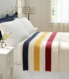 a white bed topped with pillows and a colorful blanket on top of it's headboard