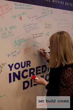 a woman writing on a white board with markers