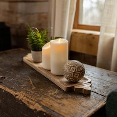 two white candles sitting on top of a wooden table next to a potted plant