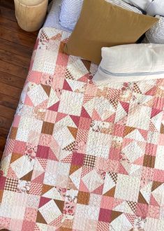 a bed with a pink and brown quilt on it's headboard next to pillows