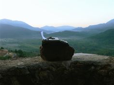 a bag sitting on top of a stone wall near mountains and valley in the distance