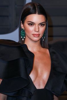 a woman with long black hair wearing green earrings